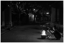 Woman burning paper on street at night. Hoi An, Vietnam ( black and white)