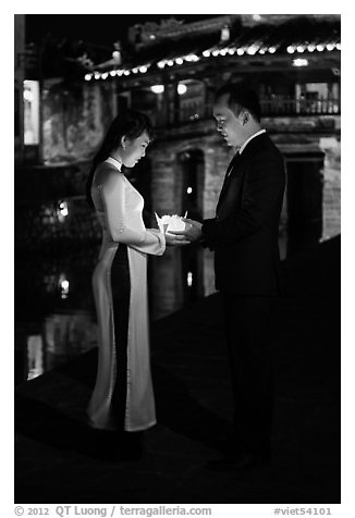 Couple holding candles in front of Japanese bridge at night. Hoi An, Vietnam (black and white)