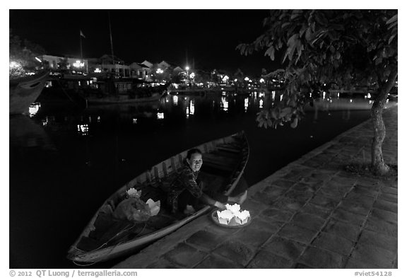 Woman sitting in rowboat selling candles on quay. Hoi An, Vietnam (black and white)