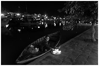 Woman sitting in rowboat selling candles on quay. Hoi An, Vietnam (black and white)