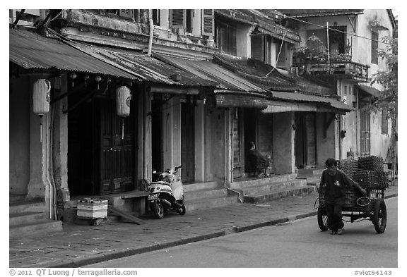 Man pulling cart in front of old townhouses. Hoi An, Vietnam