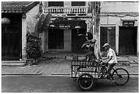 Man riding tricycle cart in front of old townhouses. Hoi An, Vietnam (black and white)