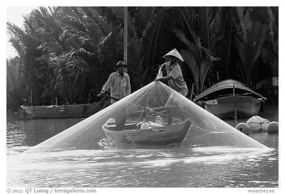 Fisherman pulls up net from rowboat. Hoi An, Vietnam (black and white)