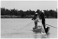 Fishermen standing in boat retrieving net, Thu Bon River. Hoi An, Vietnam (black and white)