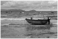 Man entering ocean with boat in stormy weather. Da Nang, Vietnam ( black and white)