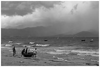 Men pushing coracle boat into stormy ocean. Da Nang, Vietnam (black and white)
