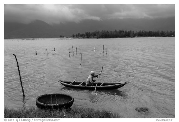 Fisherman rowing canoe in lagoon. Vietnam (black and white)