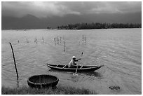 Fisherman rowing canoe in lagoon. Vietnam (black and white)