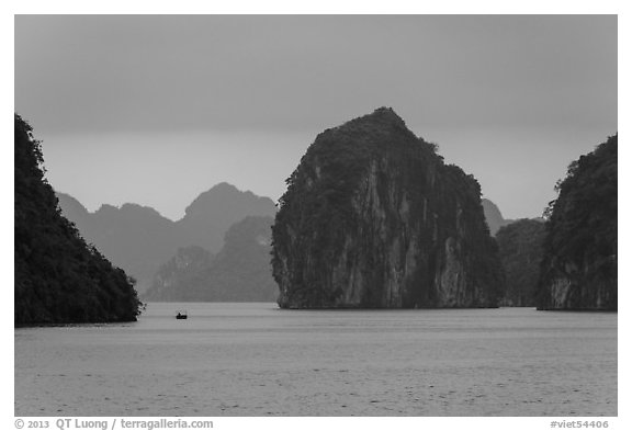 Fishing boat dwarfed by limestone islands. Halong Bay, Vietnam (black and white)