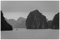 Fishing boat dwarfed by limestone islands. Halong Bay, Vietnam (black and white)