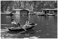 Man holding infant while rowing with feet, Vung Vieng village. Halong Bay, Vietnam (black and white)