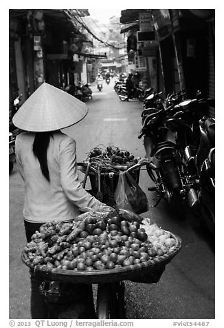 Woman pushing bicycle loaded with vegetable for sale in narrow street, old quarter. Hanoi, Vietnam
