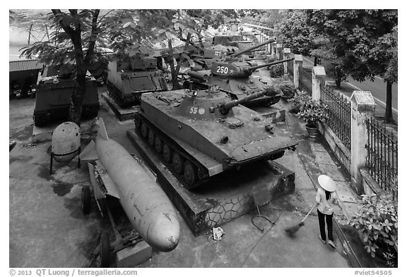 Woman sweeping floor in front of tanks, military museum. Hanoi, Vietnam (black and white)