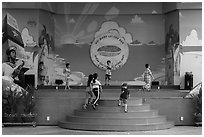 Children on stage next to militaristic mural, Dam Sen Water Park, district 11. Ho Chi Minh City, Vietnam ( black and white)