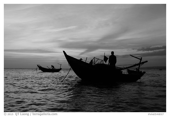 Men on fishing skiffs under bright sunset skies. Mui Ne, Vietnam (black and white)
