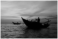 Men on fishing skiffs under bright sunset skies. Mui Ne, Vietnam ( black and white)