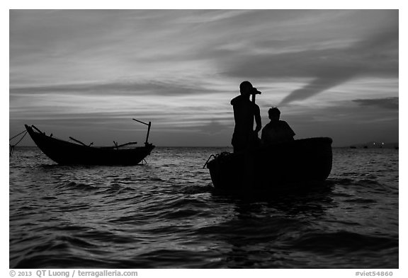 Men silhouetted paddling coracle boat at sunset. Mui Ne, Vietnam (black and white)