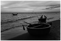 Fishermen bringing round coracle boat to shore at sunset. Mui Ne, Vietnam (black and white)