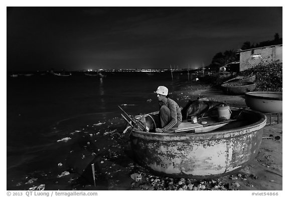 Man working on coracle boat at night. Mui Ne, Vietnam (black and white)