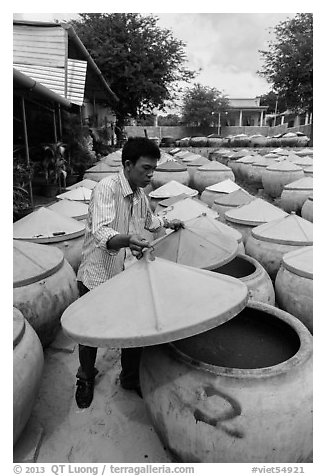 Man lifting covers of jars with fermented fish sauce. Mui Ne, Vietnam (black and white)