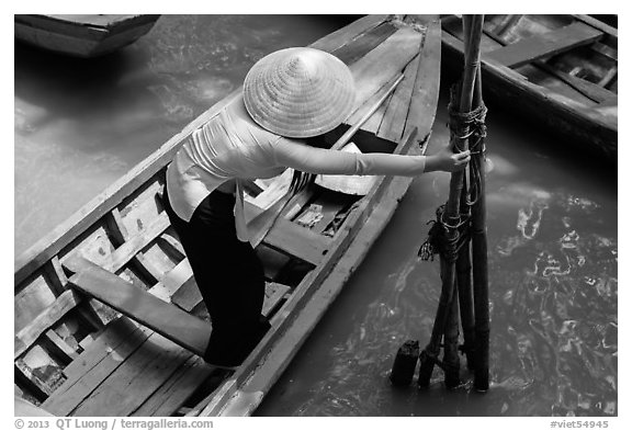 Woman in ao dai reaching to bamboo poles from boat. My Tho, Vietnam