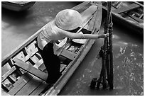 Woman in ao dai reaching to bamboo poles from boat. My Tho, Vietnam (black and white)