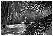 Woman paddling boat on river channel, framed by leaves. Can Tho, Vietnam (black and white)