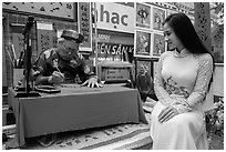 Caligrapher draws lunar new year greetings for beautiful woman in ao ai. Ho Chi Minh City, Vietnam ( black and white)