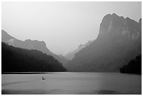 Dugout boat in Ba Be Lake, surrounded by tall cliffs, early morning. Northeast Vietnam (black and white)