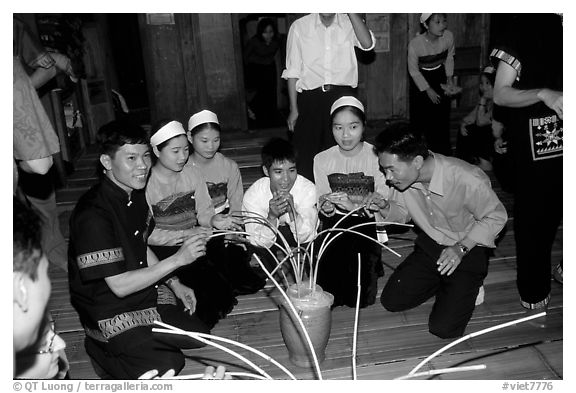 Thai women and guests drinking rau can alcohol with long straws, Ban Lac, Mai Chau. Northwest Vietnam (black and white)