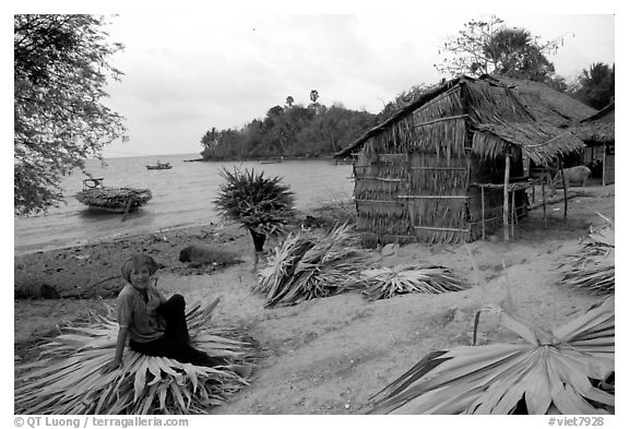 Woman taking a break sitting on leaves used to build a hut. Hong Chong Peninsula, Vietnam (black and white)