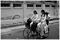 Senior high school girls ride bicycles with impeccable style, wearing elegant Ao Dai uniforms. Ho Chi Minh City, Vietnam (black and white)