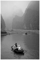 Villagers going by boat to their fields, amongst misty cliffs, Tam Coc. Ninh Binh,  Vietnam ( black and white)