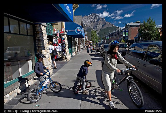 Woman and kids with mountain bikes on downtown Banff sidewalk. Banff National Park, Canadian Rockies, Alberta, Canada