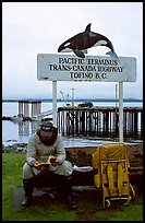 Backpacker sitting under the Transcanadian terminus sign, Tofino. Vancouver Island, British Columbia, Canada