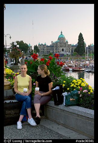 Women with shopping bags and coffee cups at the Inner Harbour, sunset. Victoria, British Columbia, Canada (color)