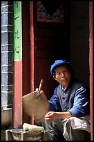 Naxi woman at doorway selling broiled corn. Lijiang, Yunnan, China (color)