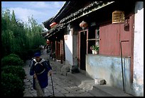 Naxi woman sweeps the floor at the door of her wooden house. Lijiang, Yunnan, China (color)
