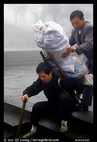 Porter getting helped to shoulder a heavy load on a back frame. Emei Shan, Sichuan, China (color)