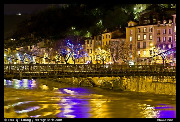 Suspension bridge at night with Christmas lights reflected in river. Grenoble, France