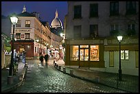 Cobblestone street, lamps, and Sacre-Coeur basilica by night, Montmartre. Paris, France
