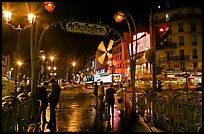 Metro entrance, boulevard, and Moulin Rouge on rainy night. Paris, France