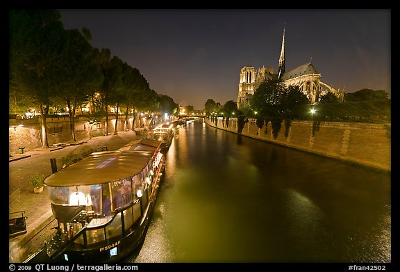 Quay, lighted boats, Seine River and Notre Dame at night. Paris, France