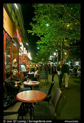 Couple walking by outdoor tables of cafe at night. Paris, France