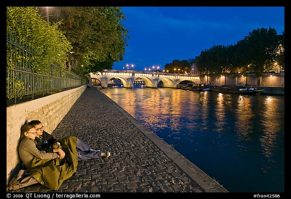 Couple sitting on quay on banks of the Seine River. Paris, France
