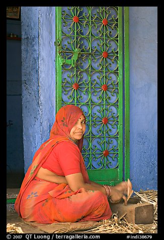 Woman in orange sari sitting next to green door and blue wall. Jodhpur, Rajasthan, India (color)