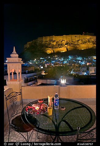 Rooftop restaurant table with food served and view of Mehrangarh Fort by night. Jodhpur, Rajasthan, India