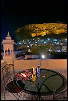 Rooftop restaurant table with food served and view of Mehrangarh Fort by night. Jodhpur, Rajasthan, India ( color)