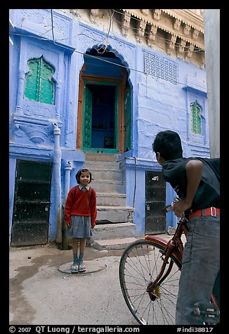 Boy on bicycle looking at girl in front of blue house. Jodhpur, Rajasthan, India