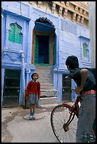 Boy on bicycle looking at girl in front of blue house. Jodhpur, Rajasthan, India (color)